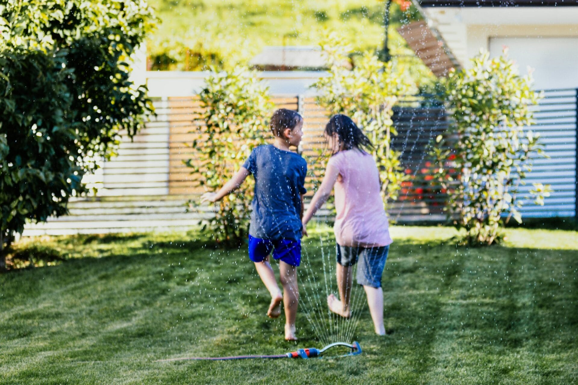 Family fun with lawn sprinkler in summertime. Children jumping over lawn sprinkler.